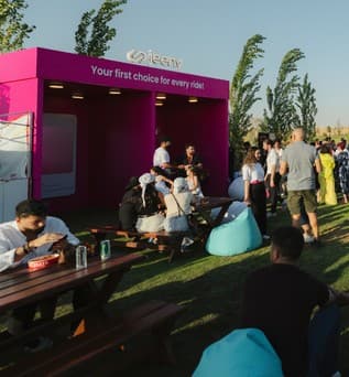 A bright pink partner booth on the lawn with guests sitting at picnic tables in front of it.
