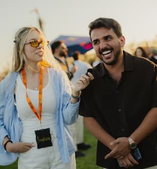 Two creators share a microphone and laugh together at sunset.