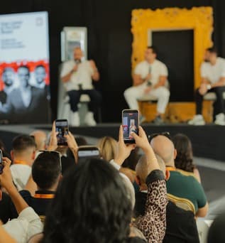 A panel of three speakers on the main stage, framed by the gold Jordan Create frame, while the audience films on their phones.