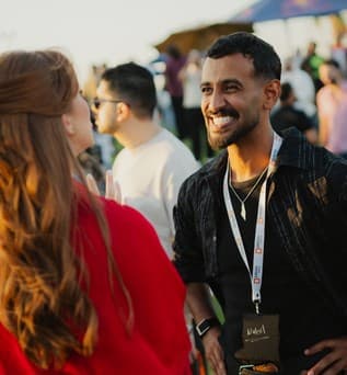 Two guests with lanyards laughing together outdoors at golden hour.