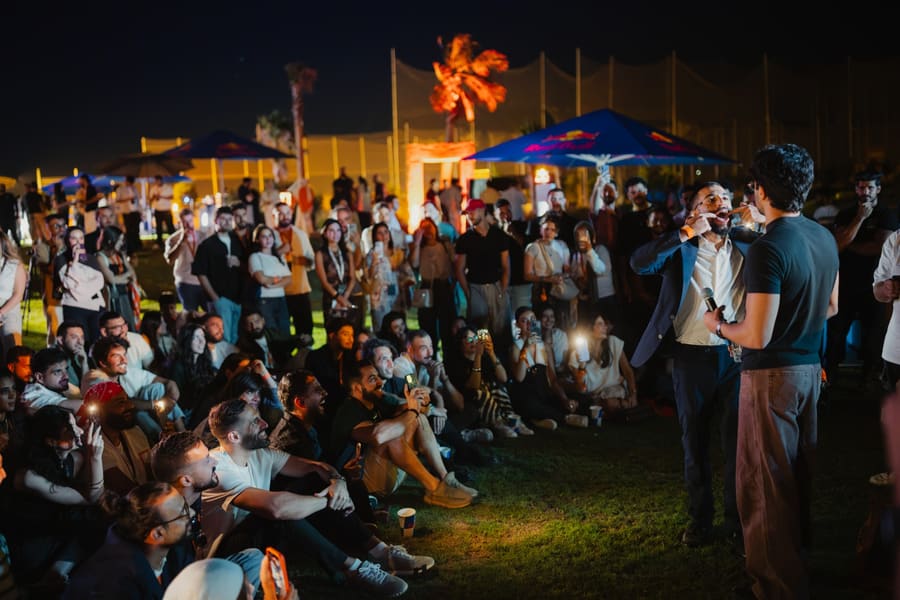 A crowd sitting on the lawn at night, phones lit, watching a magician perform at Jordan Create Volume 2
